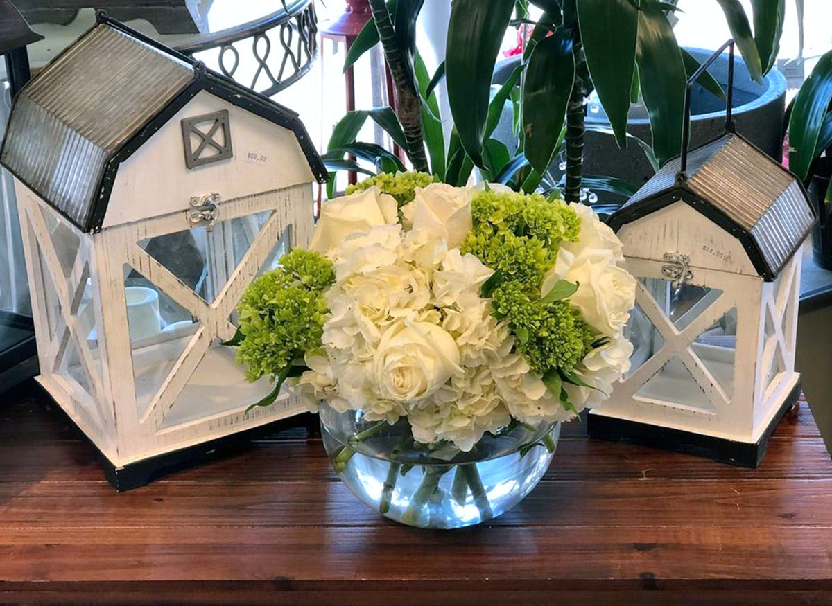 A simple white and green arrangement, seen alongside a pair of quaint, barn-themed candle holders